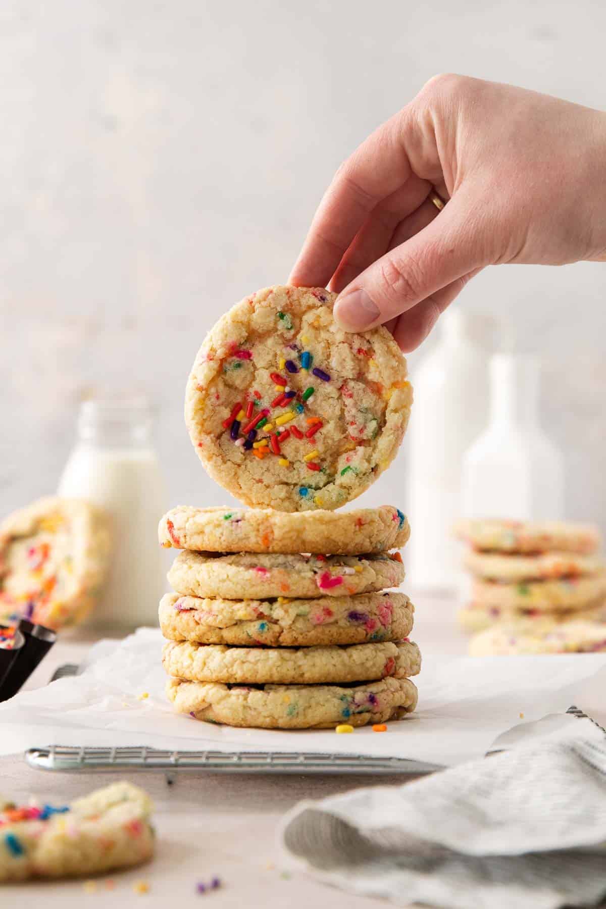 A stack of sugar cookies on parchment paper, with a hand picking up the top cookie