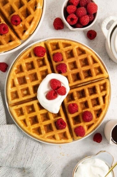 gluten-free waffles on a plate with whipped cream and raspberries