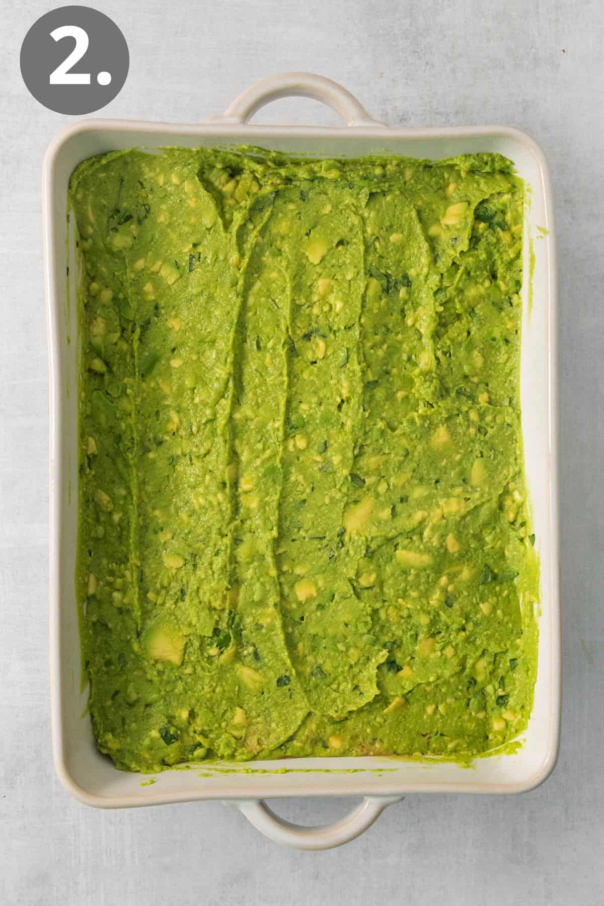 Guacamole layered on top of beans in a baking dish