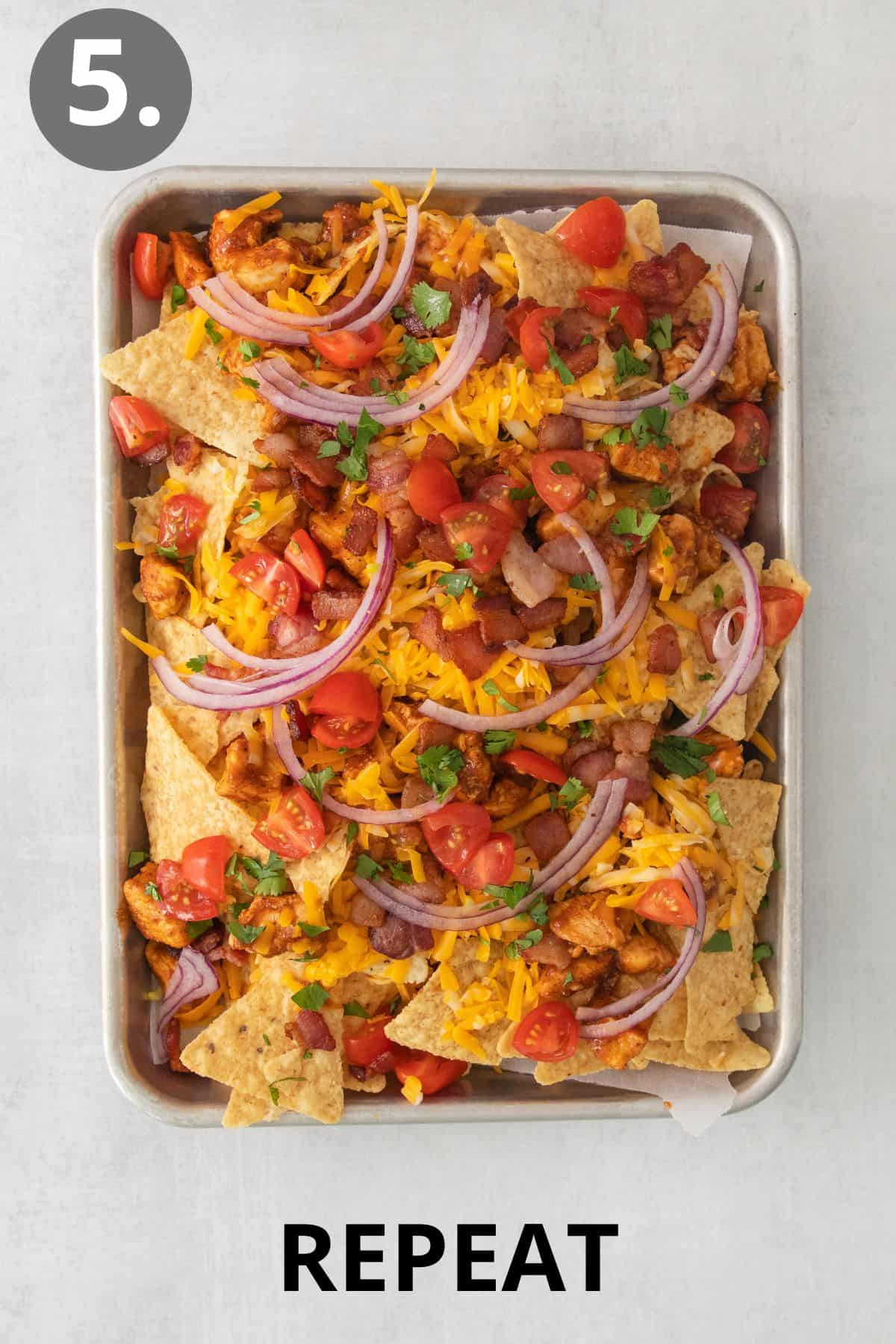 Additional layers of nacho ingredients layered on a sheet pan