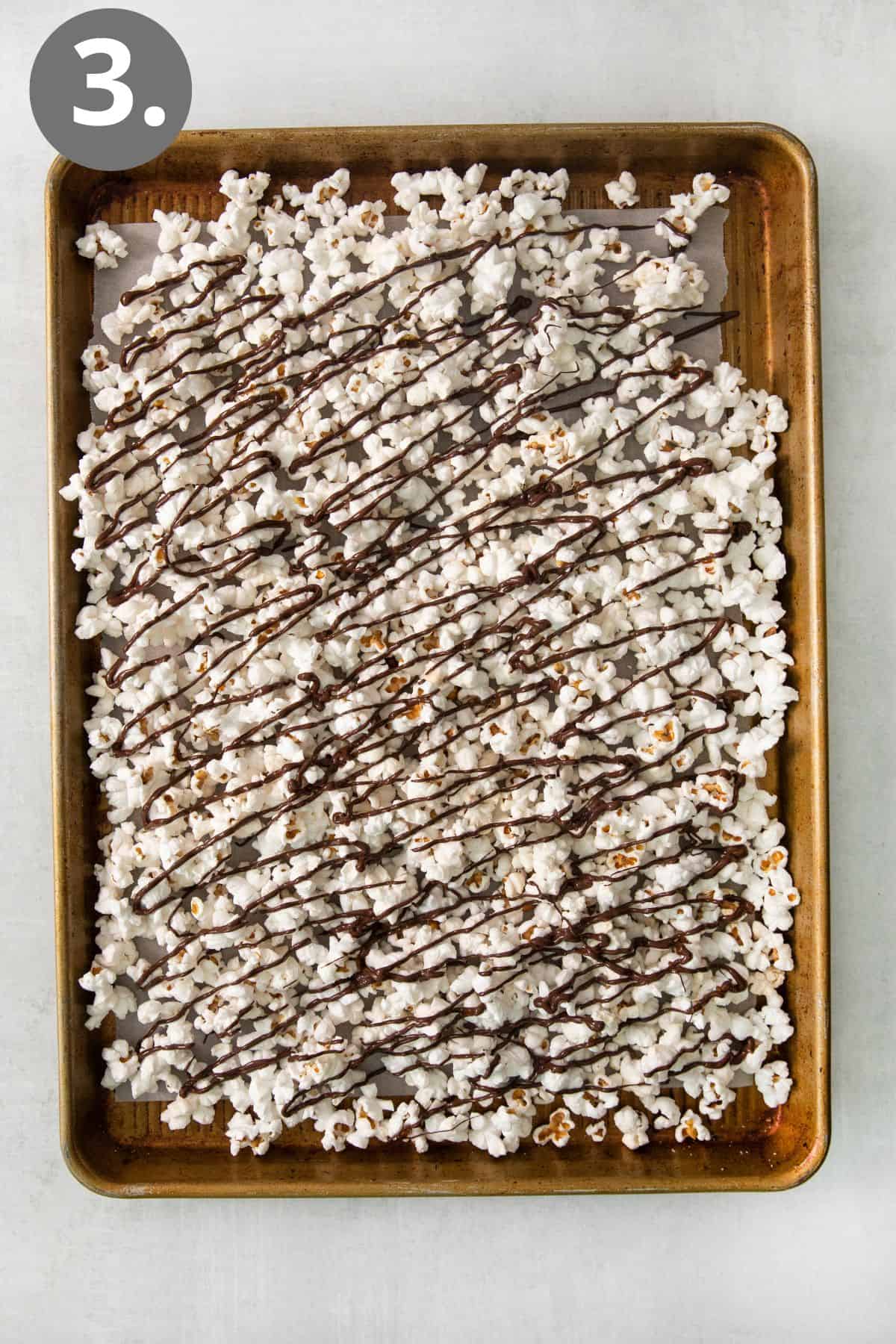 Chocolate drizzle popcorn on a baking sheet