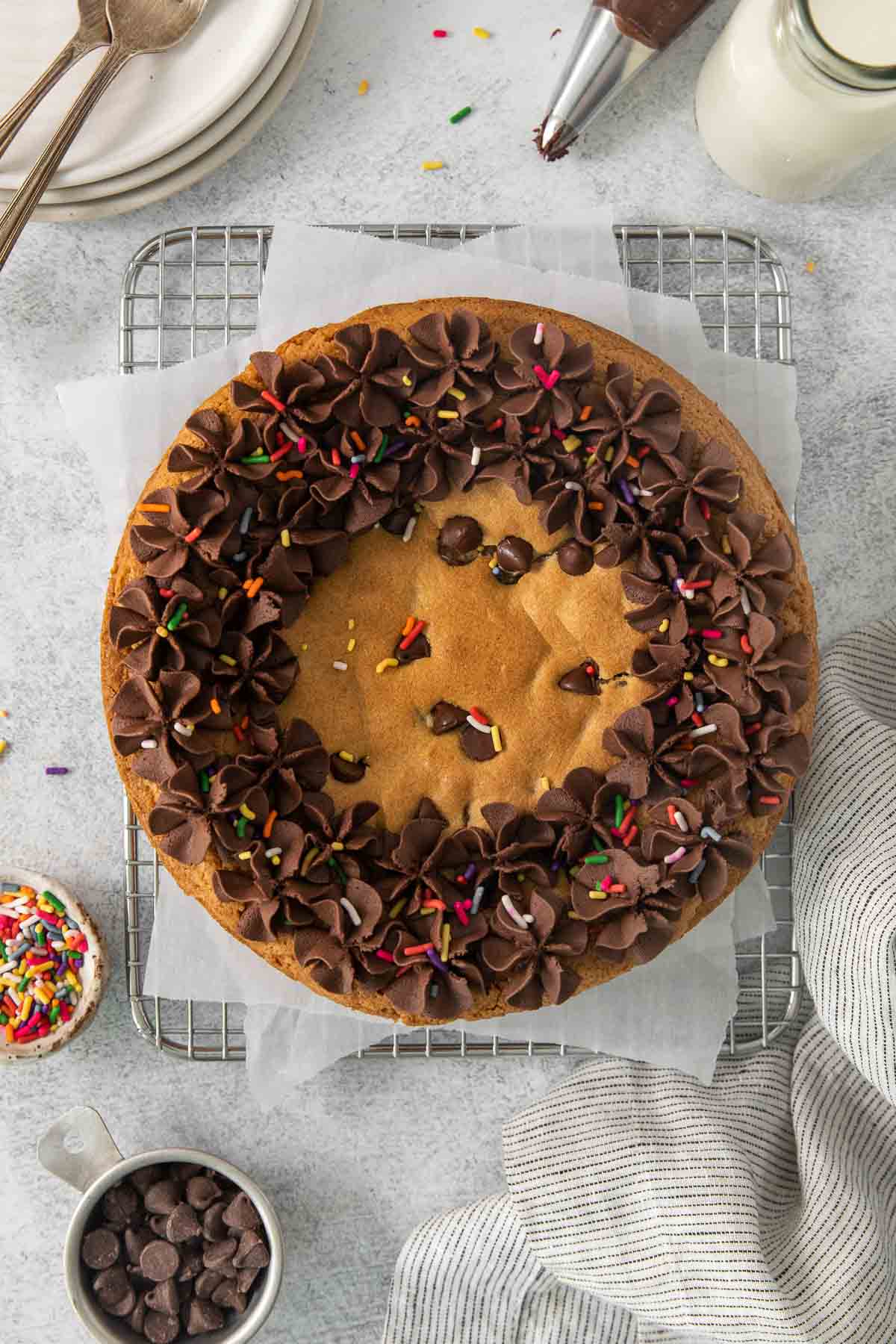 overhead shot of cookie cake on cooling rack with chocolate frosting and sprinkles