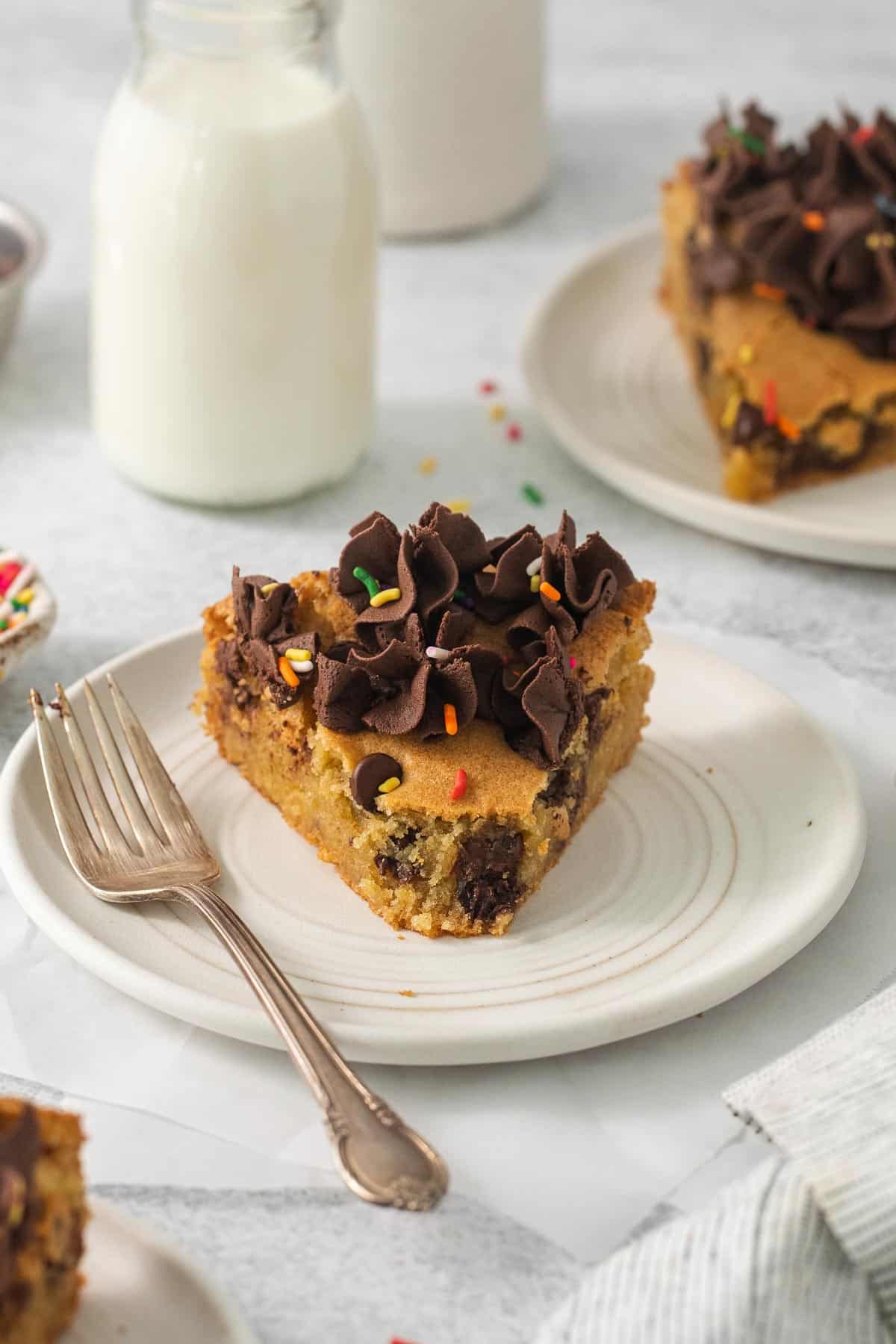Cookie cake on a plate with a fork and milk in the background