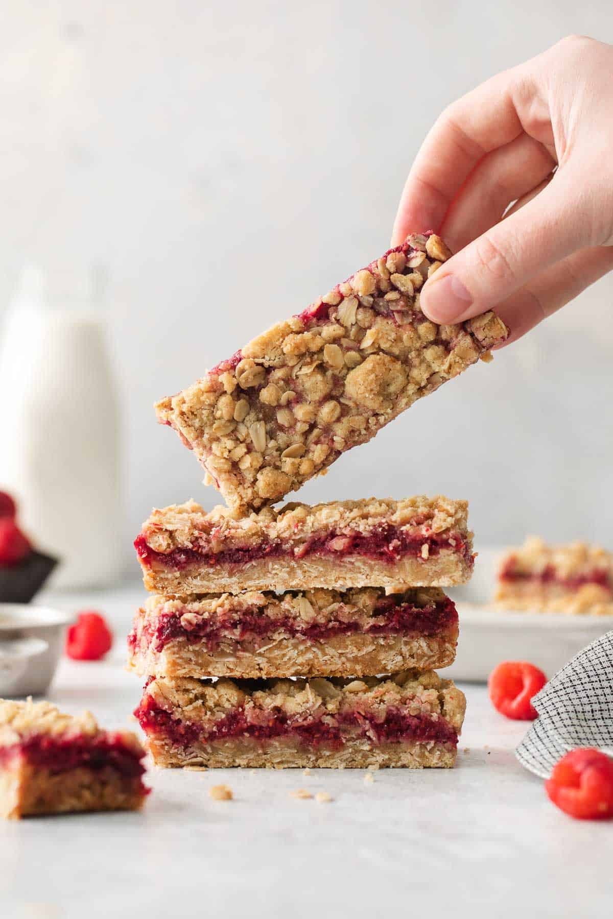 Gluten-free raspberry bars stacked on top of each other and a hand picking up the top bar