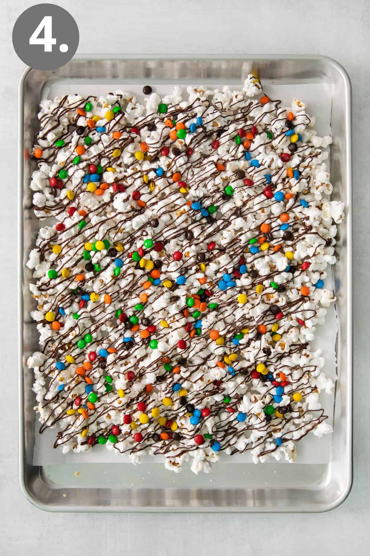 Popcorn on a baking sheet with melted chocolate and M&Ms