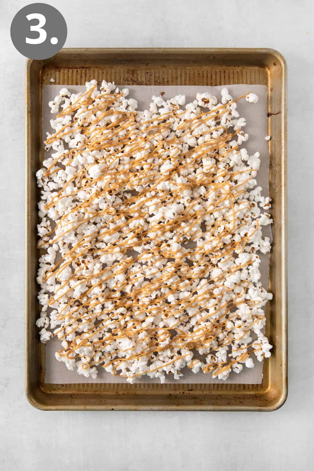 Peanut butter drizzled over popcorn that is on a sheet pan