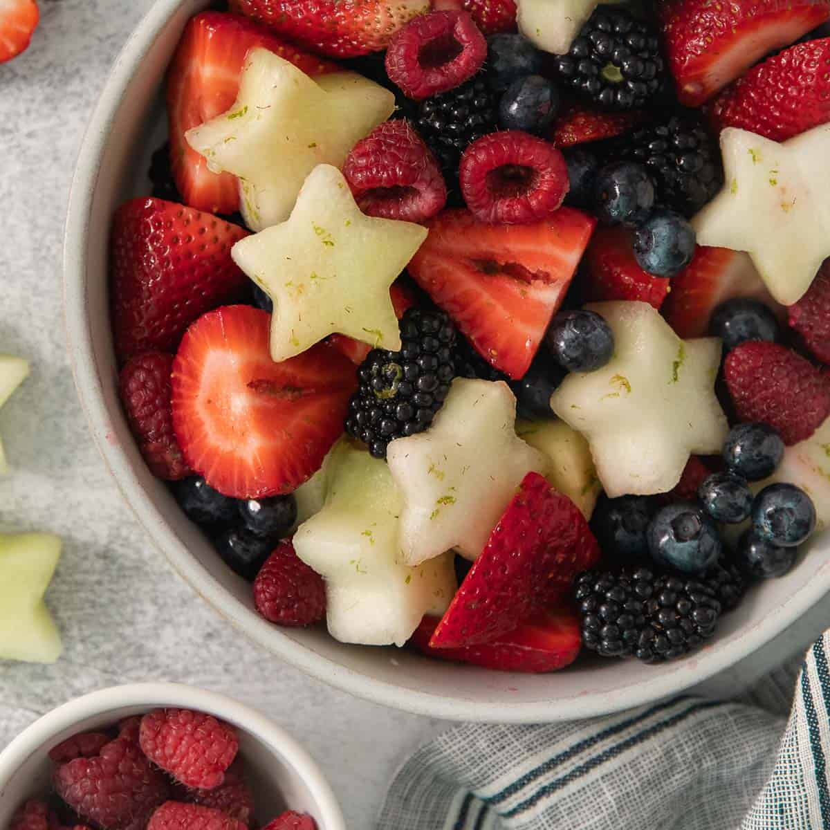 Fourth of July fruit salad in a bowl with fruit surrounding it