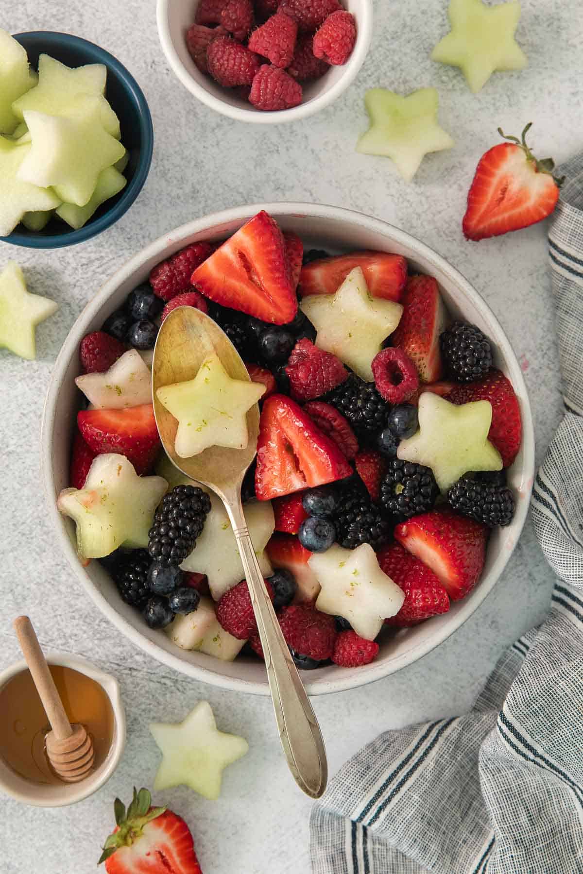Fourth of July fruit salad in a bowl with fruit surrounding it and spoon scooping some out