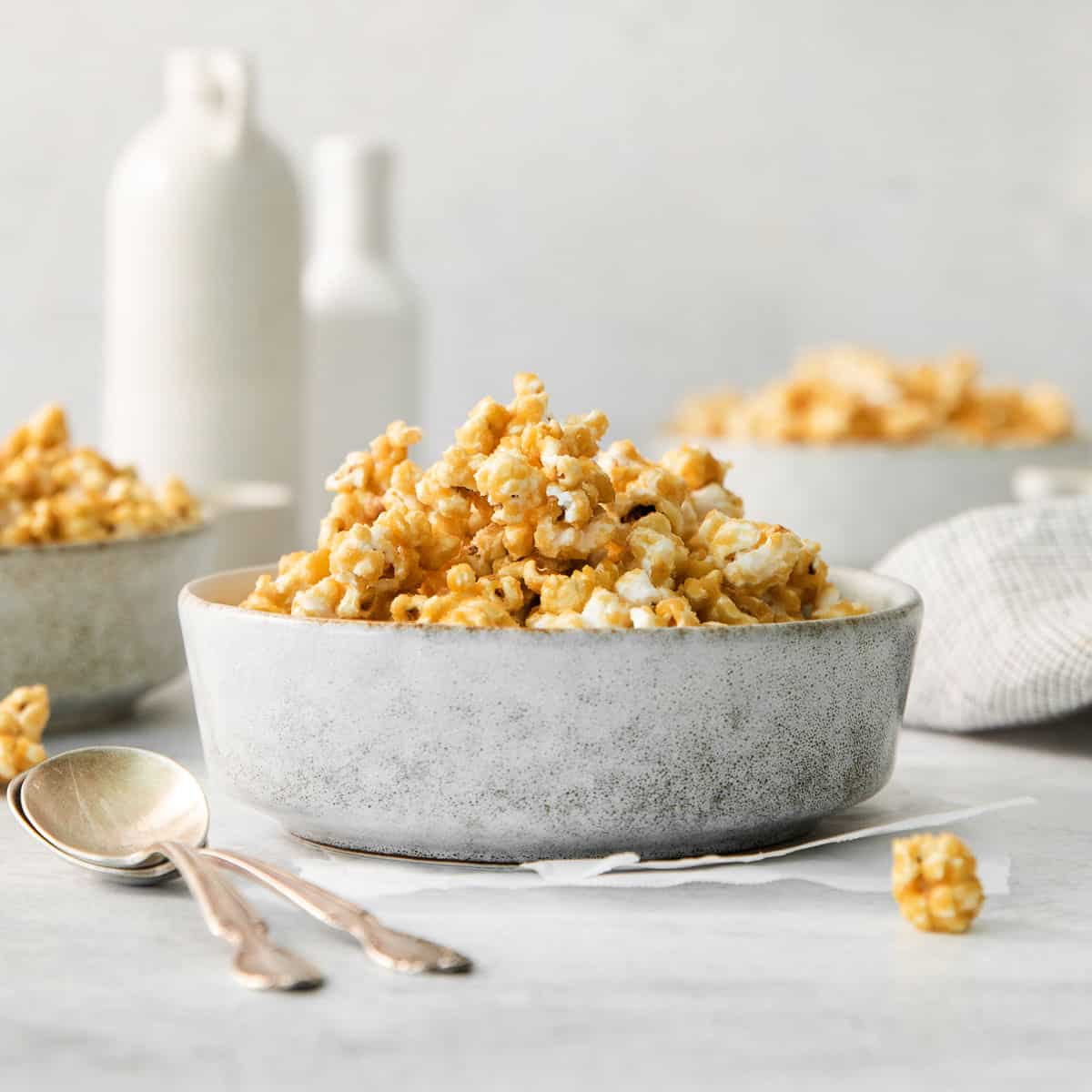 Microwave caramel corn in a bowl on a countertop, with bowls of popcorn and jars of milk in the background