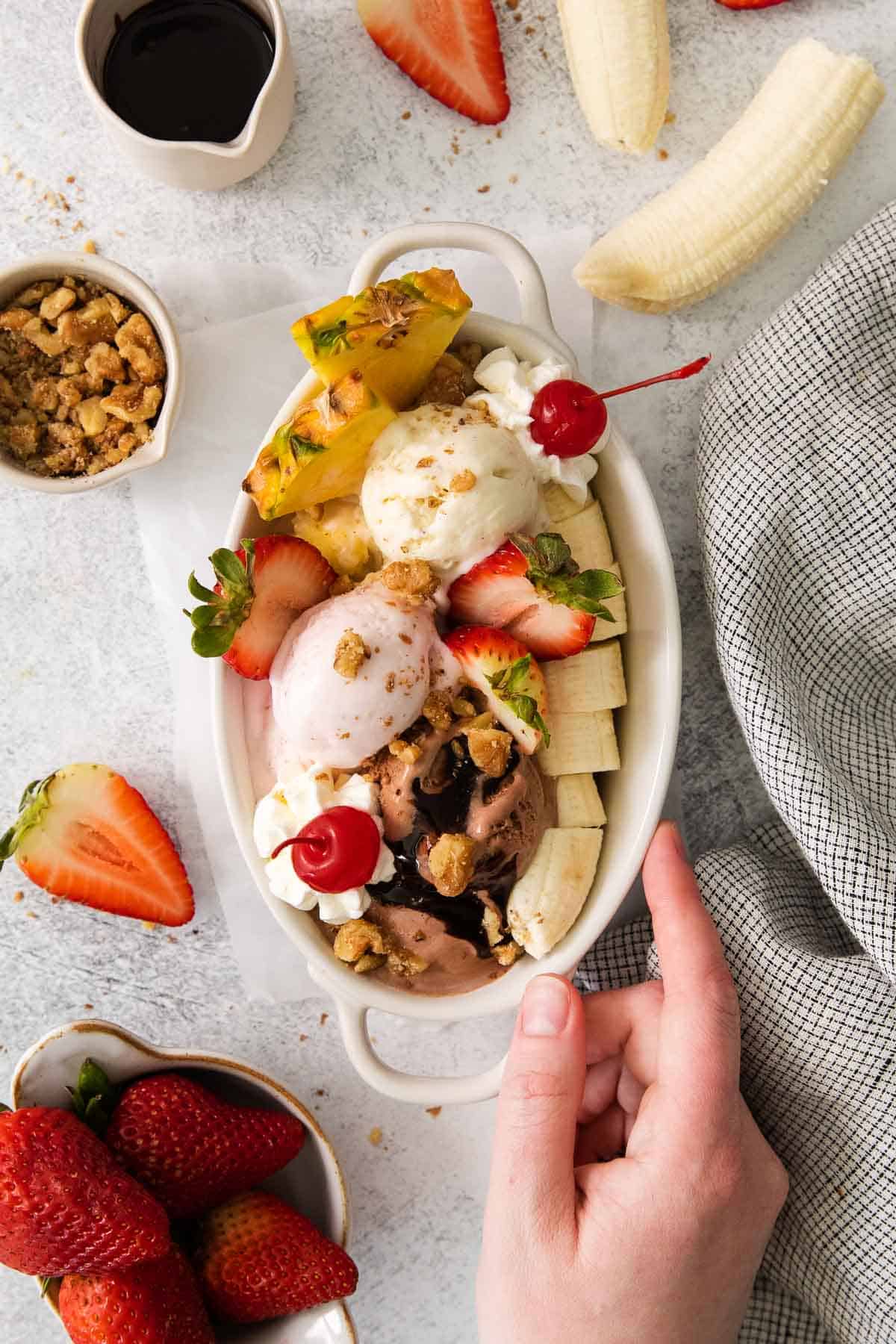 Banana split in a dish with a hand touching the dish