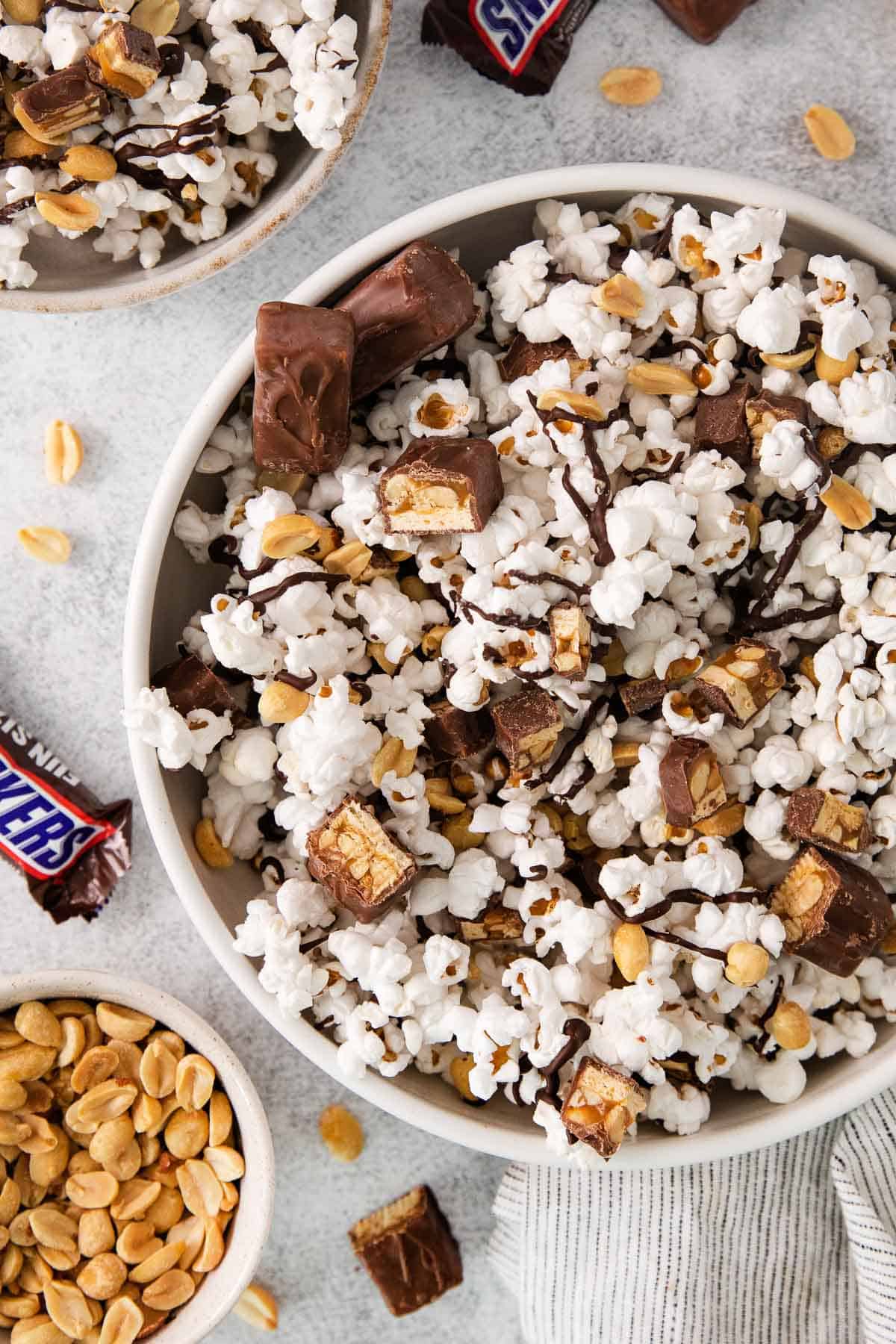 Snickers popcorn in a bowl with a Snickers bar and peanuts on the side