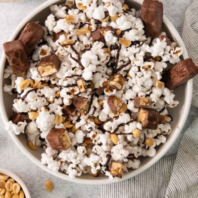 Snickers popcorn in a bowl with a Snickers bar and peanuts on the side