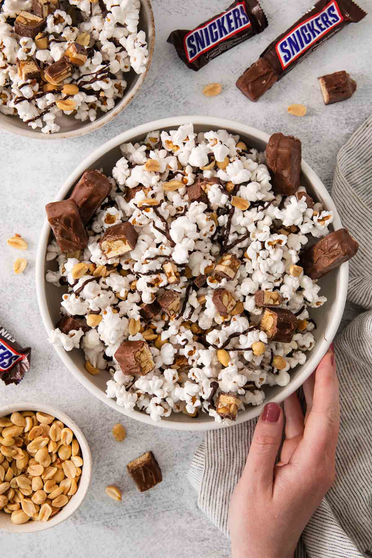 Snickers popcorn in a bowl with a hand touching the bowl