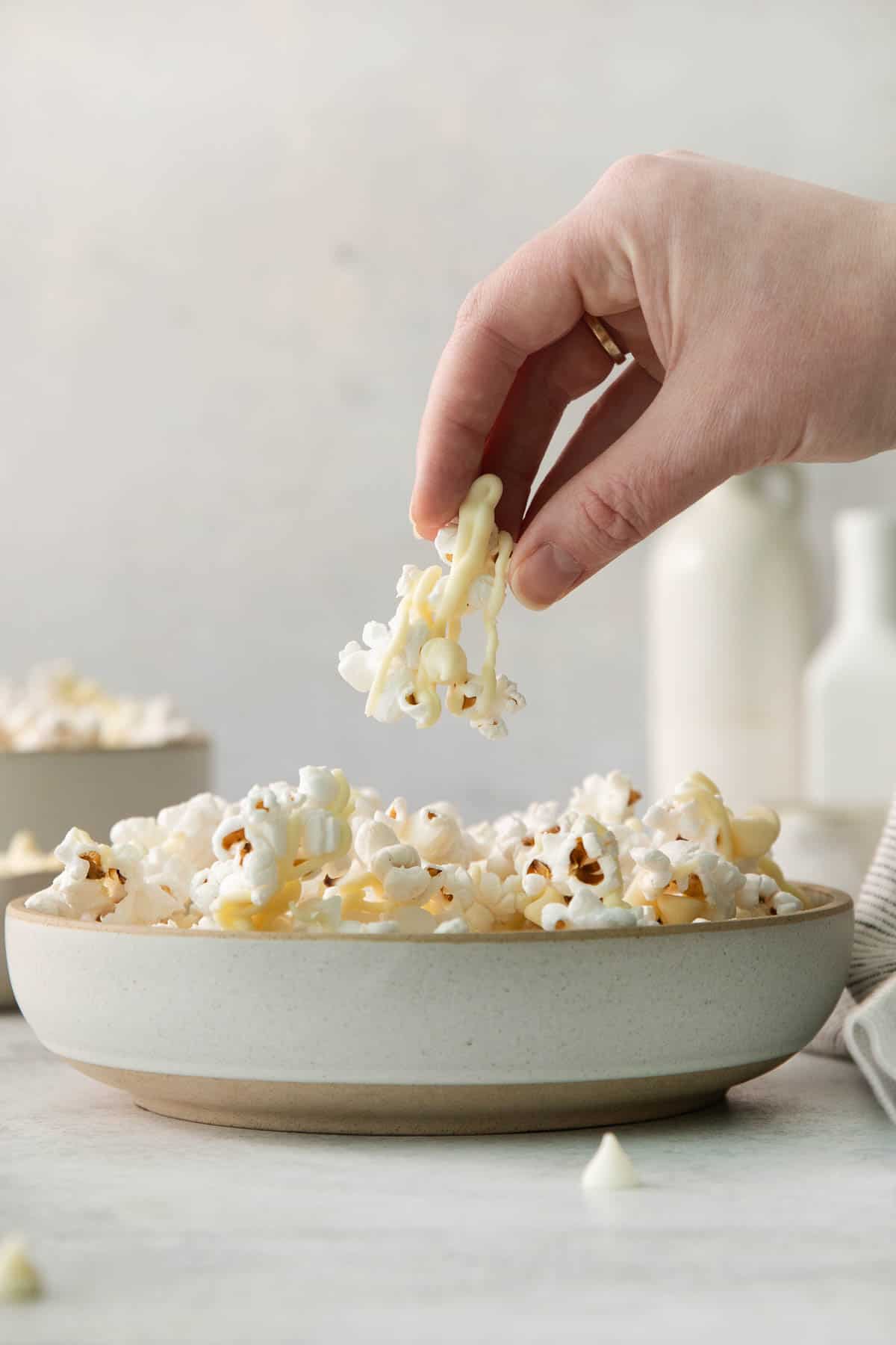 White chocolate popcorn in a bowl and a hand picking up a piece