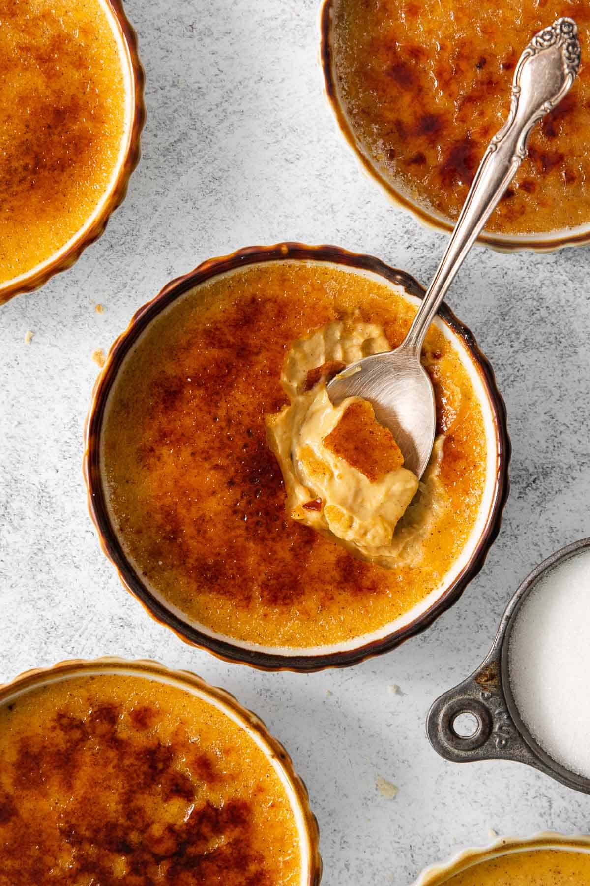 Pumpkin creme brulee in ramekins on a countertop, with a spoon in the ramekin
