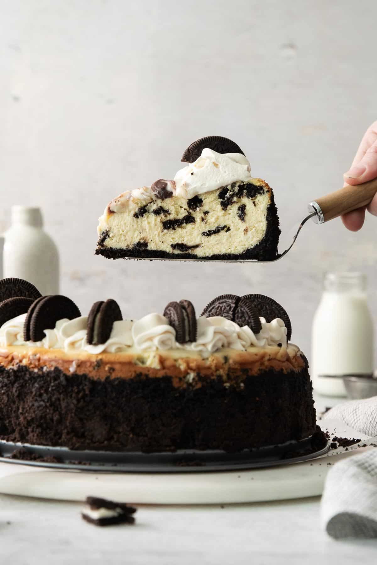 A hand lifting a slice of gluten-free Oreo cheesecake off of a platter