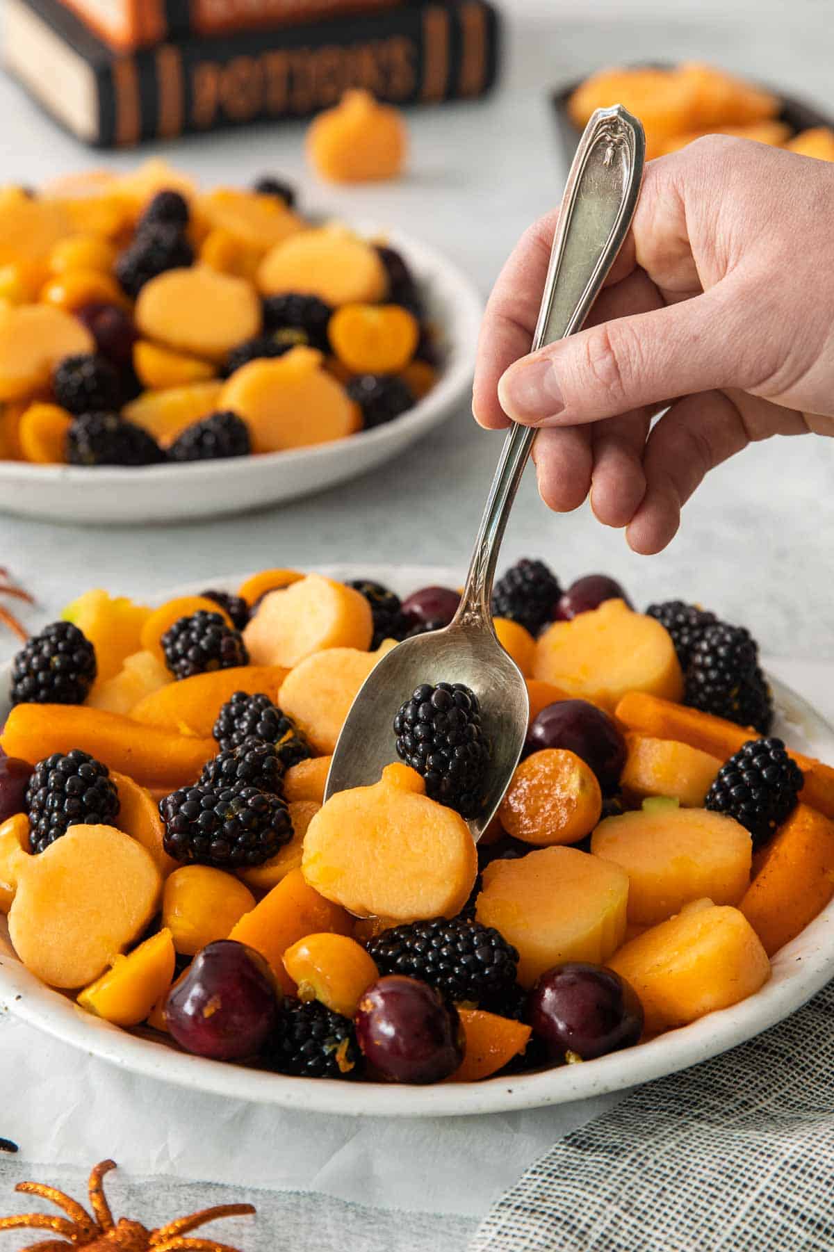 A hand holding a serving spoon to scoop into the bowl of Halloween fruit salad
