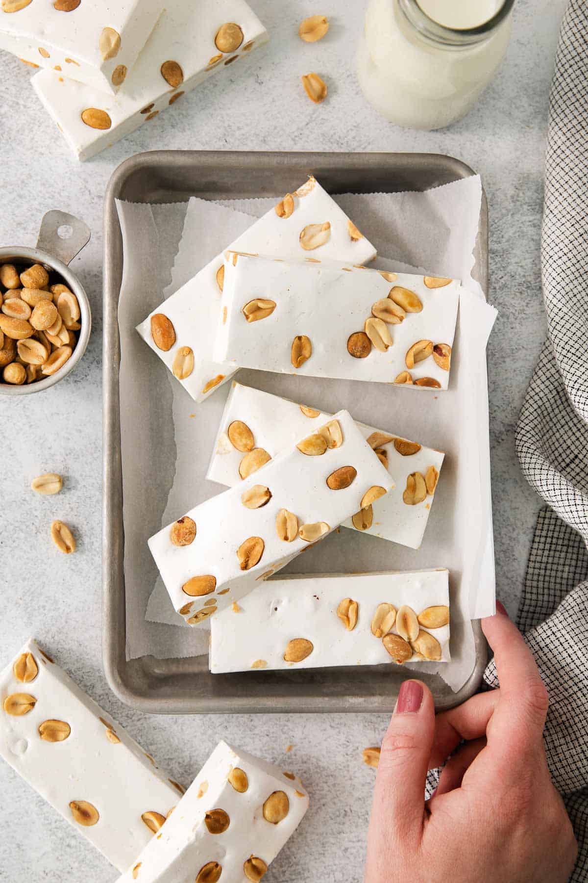 Nougat recipe on a baking sheet with parchment paper and a hand touching the baking sheet