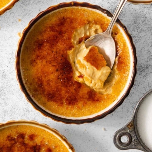 Pumpkin creme brulee in ramekins on a countertop, with a spoon in the ramekin