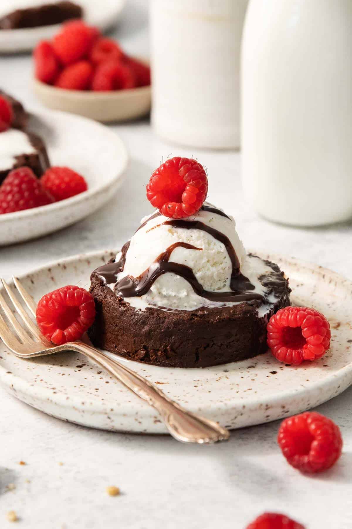 gluten-free chocolate lava cake on a plate with raspberries and a scoop of vanilla ice cream