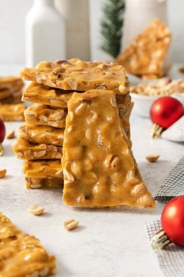 peanut brittle stacked on a countertop with ornaments in the background
