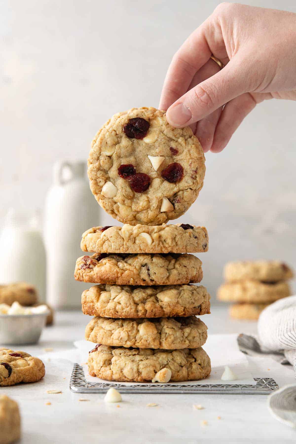 A stack of gluten-free white chocolate cranberry cookies on a countertop with a hand picking up the top cookie