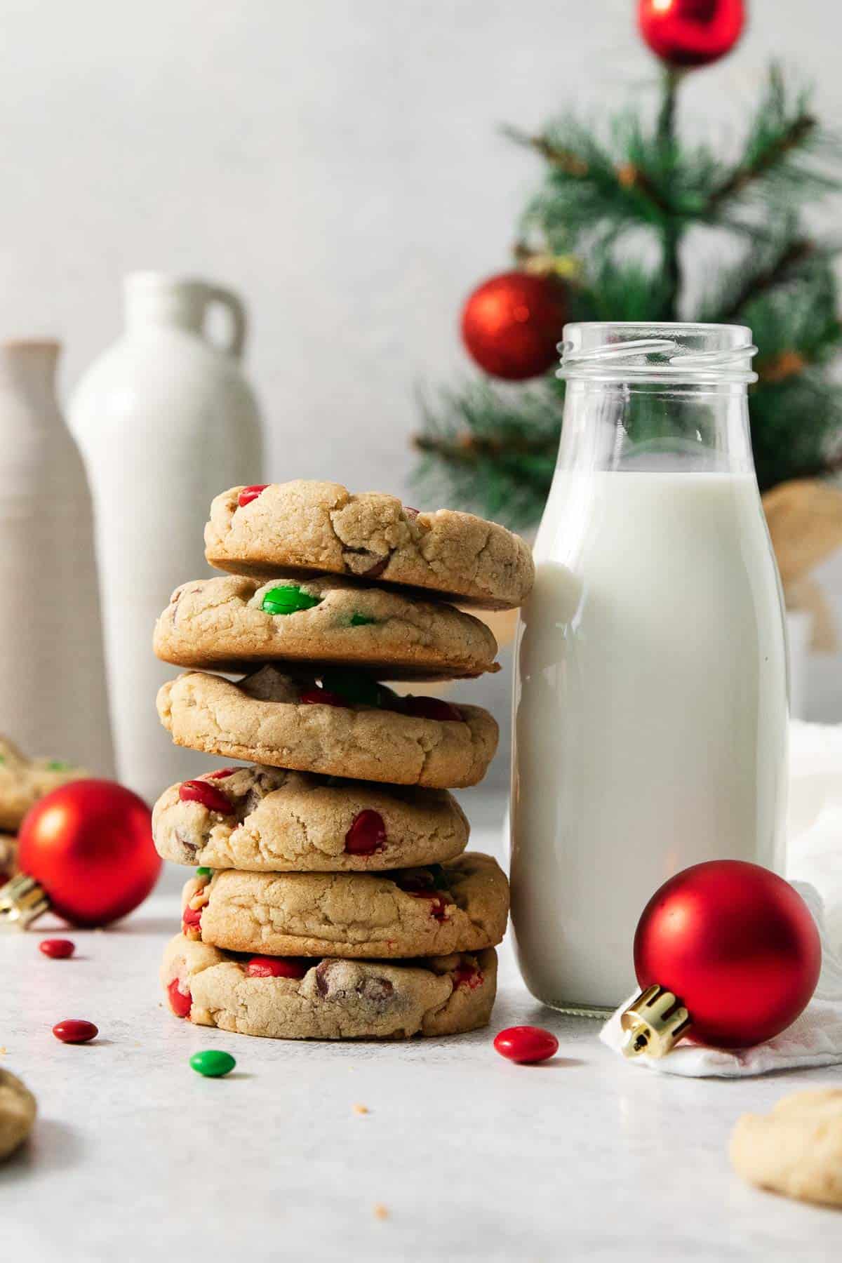 gluten-free M&M cookies stacked on a countertop with milk in a jar next to it