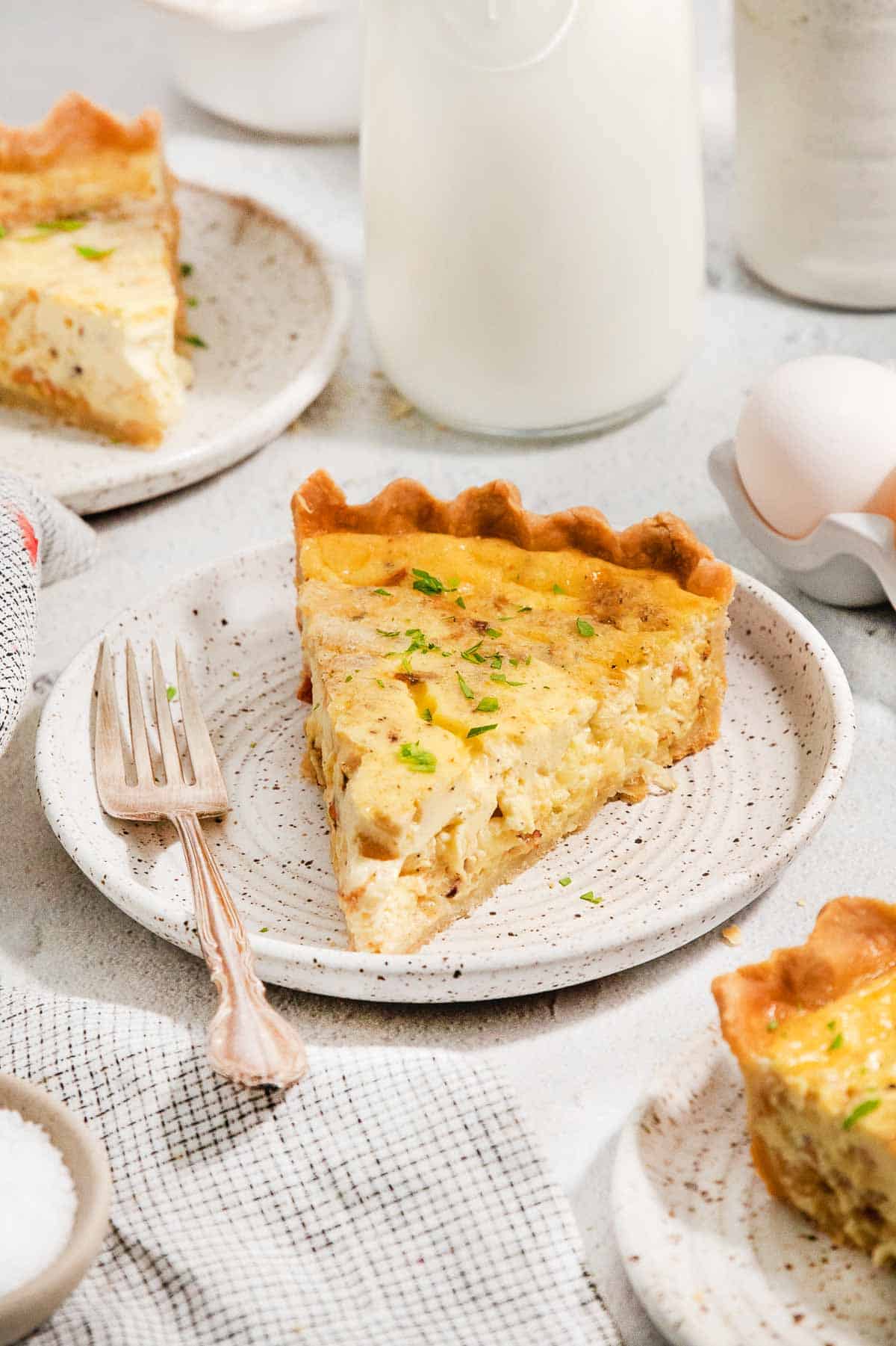 a slice of gluten-free quiche lorraine on a plate with a fork next to it
