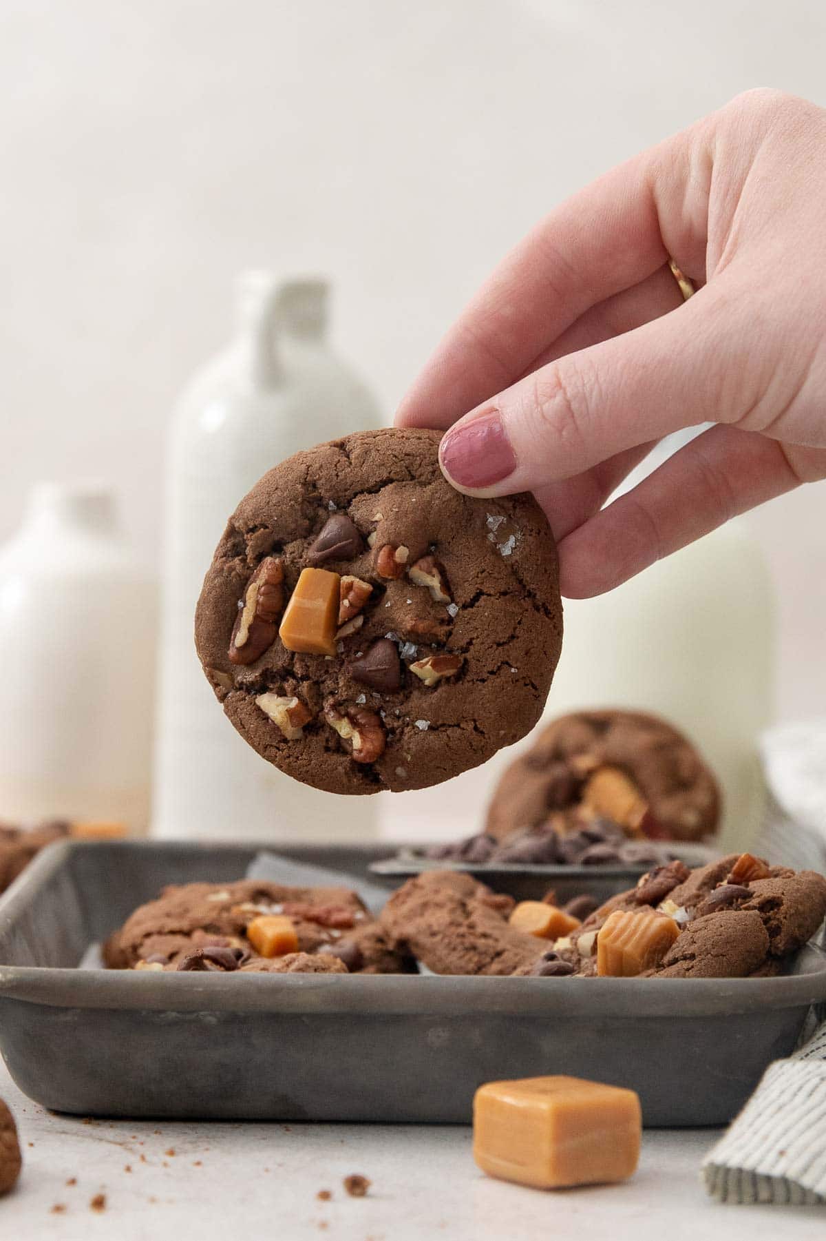a hand holding up one chocolate turtle cookie above the pan of cookies.