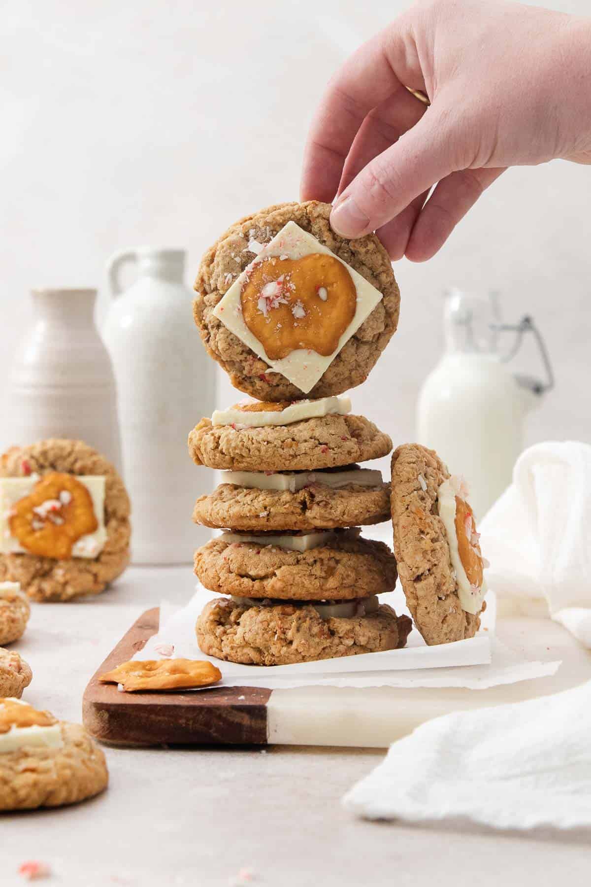 a hand holding up one white chocolate peppermint pretzel cookie on top of a stack.