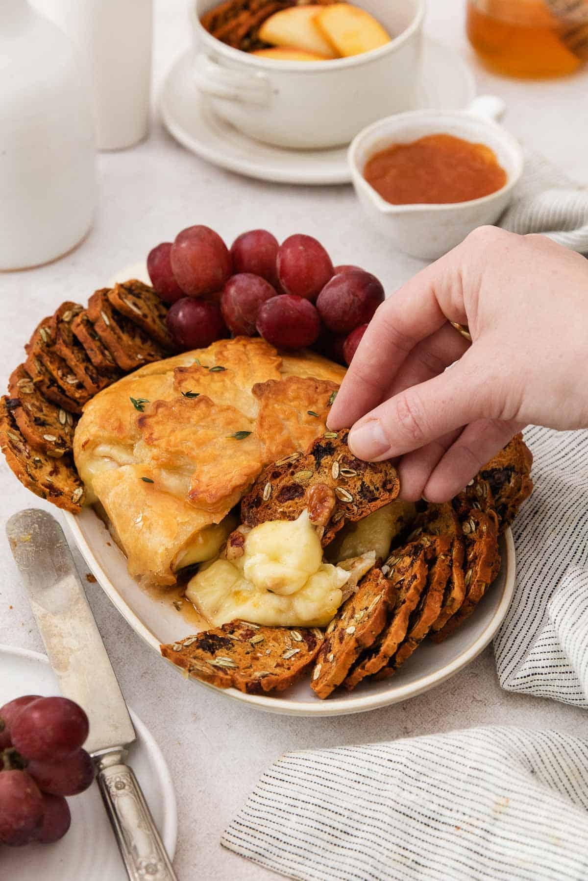 A hand dipping a cracker into gluten-free baked Brie.