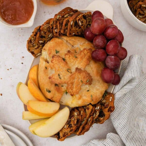 A square photo of gluten-free baked Brie on a platter with gluten-free crackers and grapes.