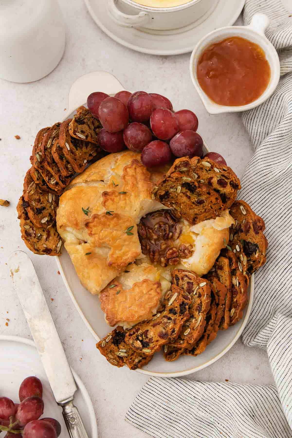 Gluten-free baked brie on a platter with gluten-free crackers and grapes.