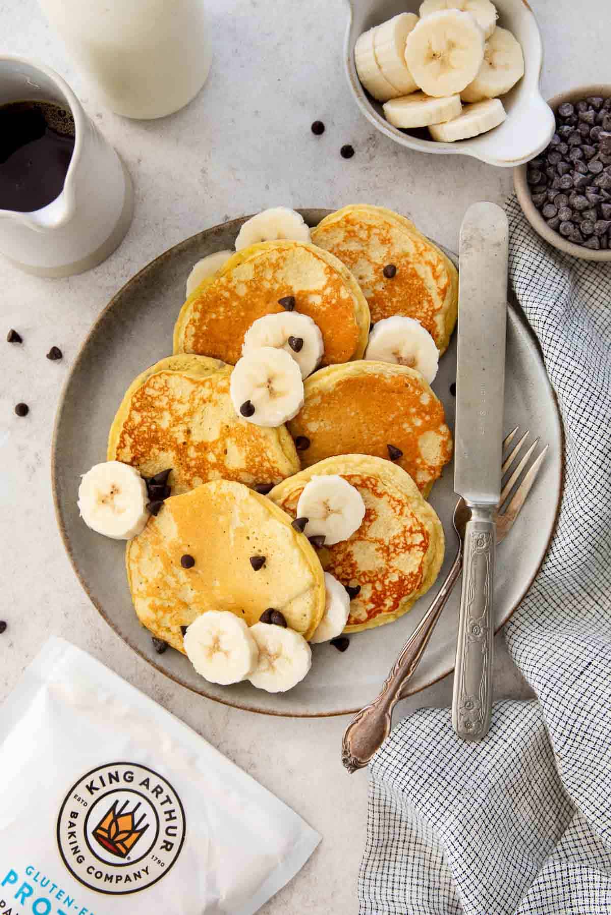 Gluten-free banana protein pancakes on a plate with chocolate chips and banana slices.