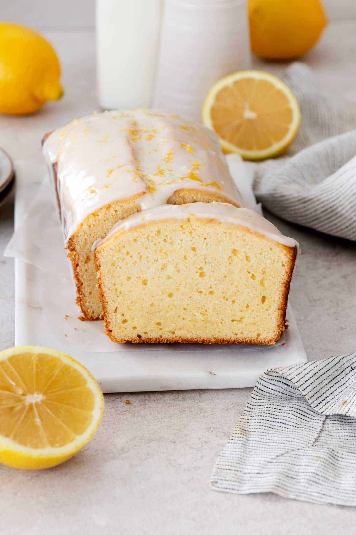 Sliced gluten-free lemon loaf on a marble serving tray with lemons around it.