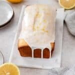 Sliced gluten-free lemon loaf on a marble serving tray with lemons around it.