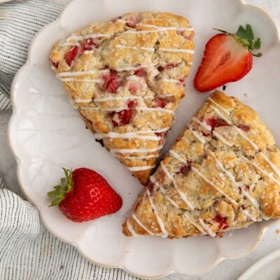 two strawberry scones on a white scalloped plate with two strawberries.