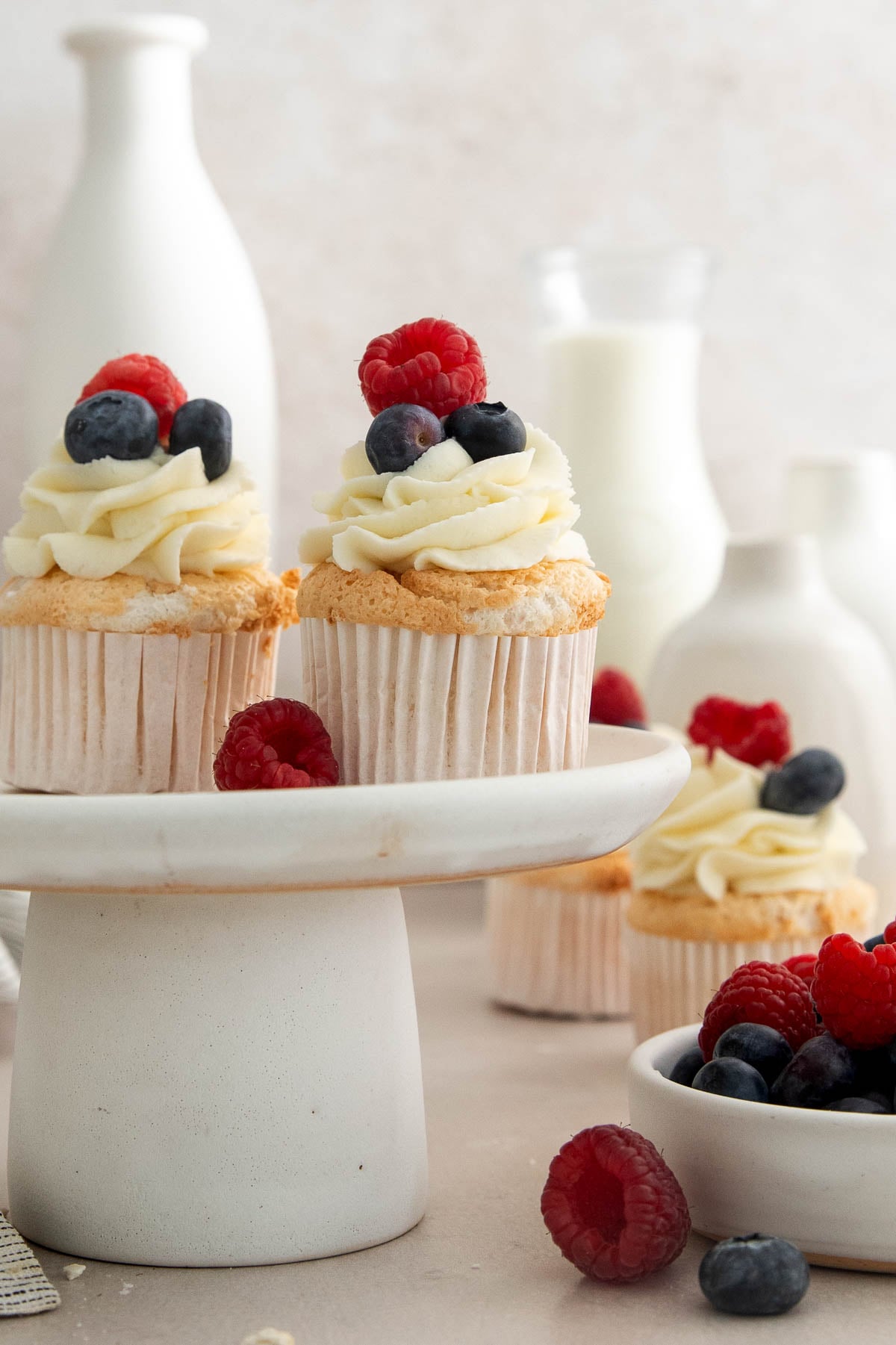 angel food cake cupcakes topped with mascarpone whipped cream and berries on a cake stand.