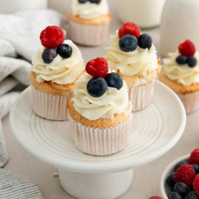 three angel food cake cupcakes topped with berries on a cake stand.
