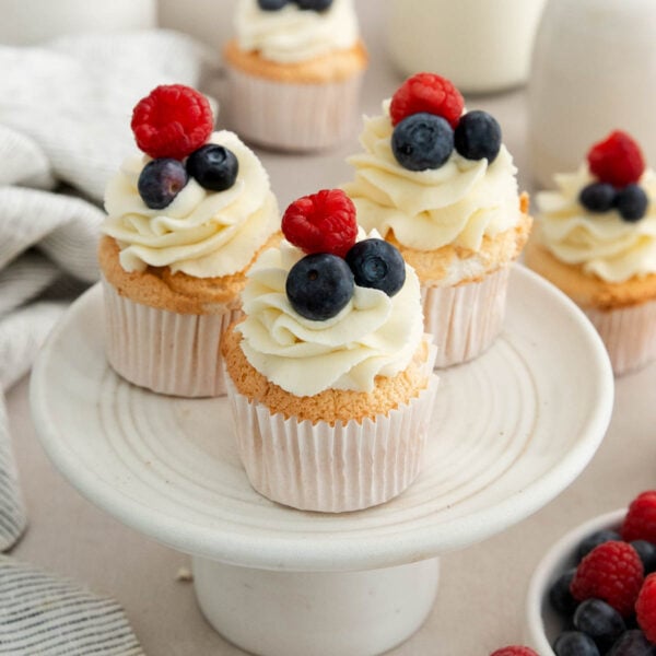 three angel food cake cupcakes topped with berries on a cake stand.