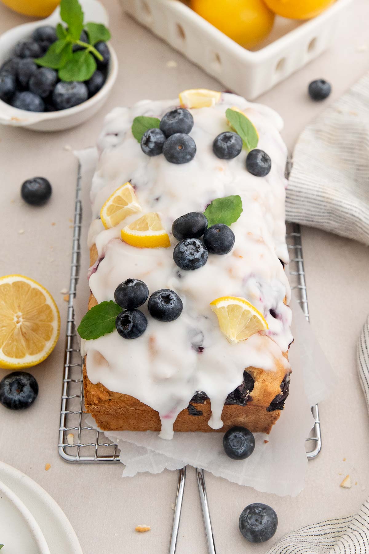 a glazed lemon blueberry bread topped with fruit on a parchment lined wire rack.