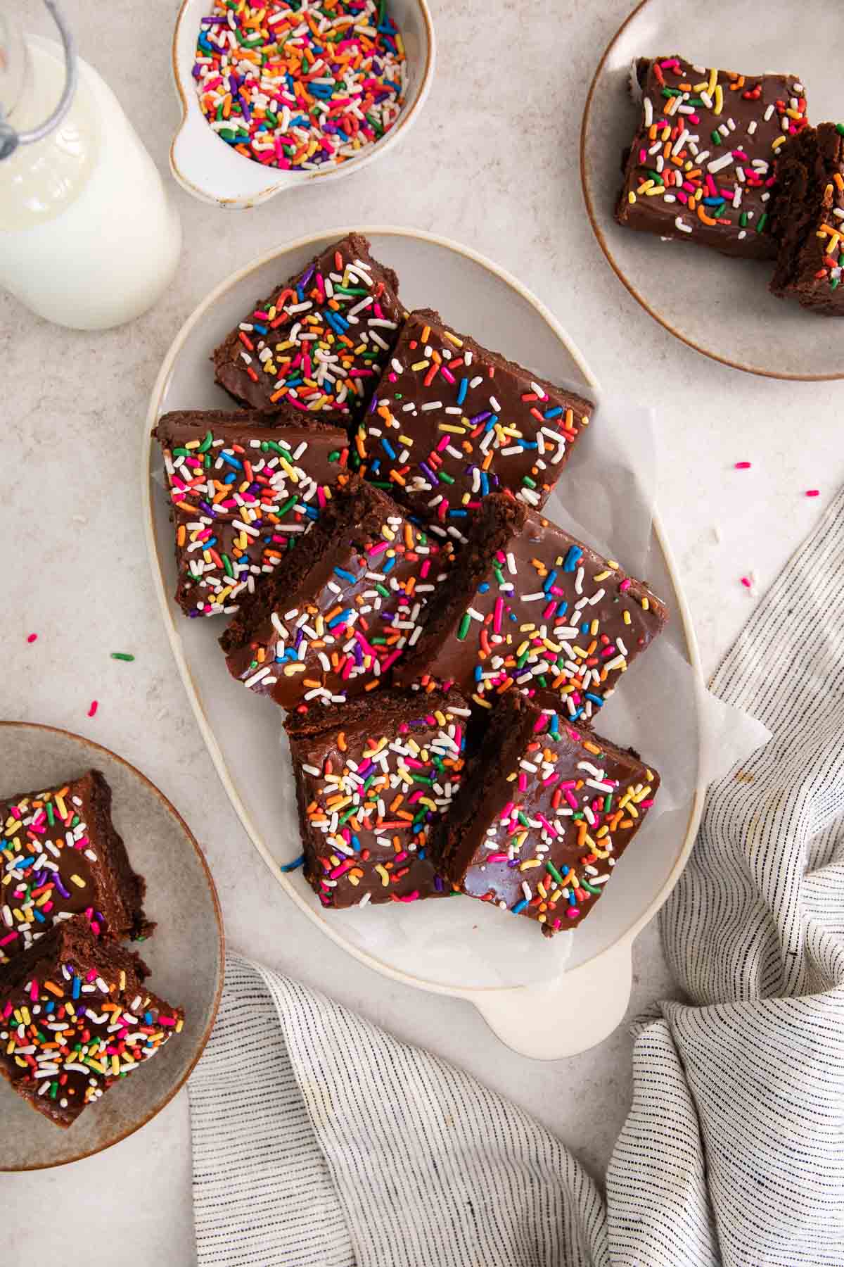 sliced brownies topped with fudge frosting and rainbow sprinkles on a platter.
