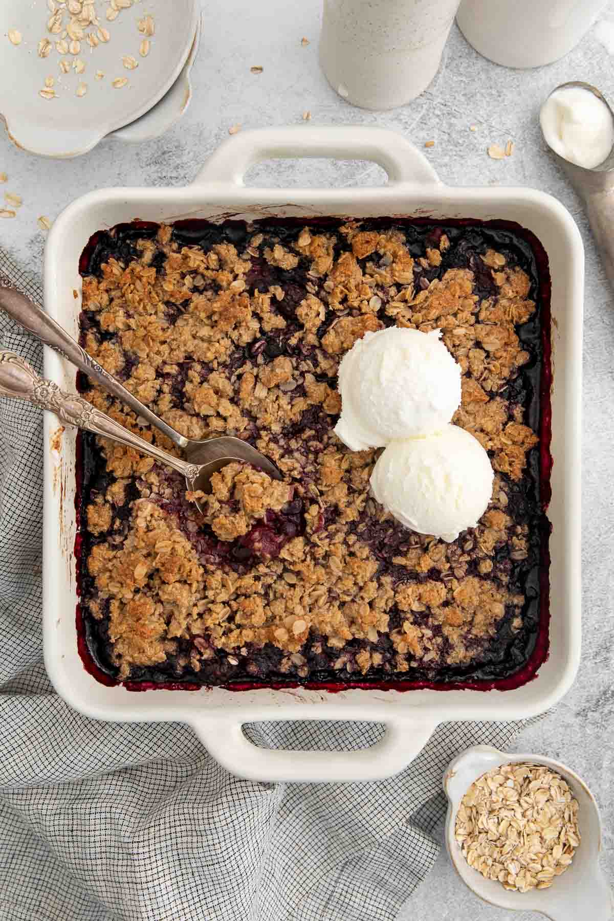 triple berry crisp in a white baking dish with ice cream and two spoons.