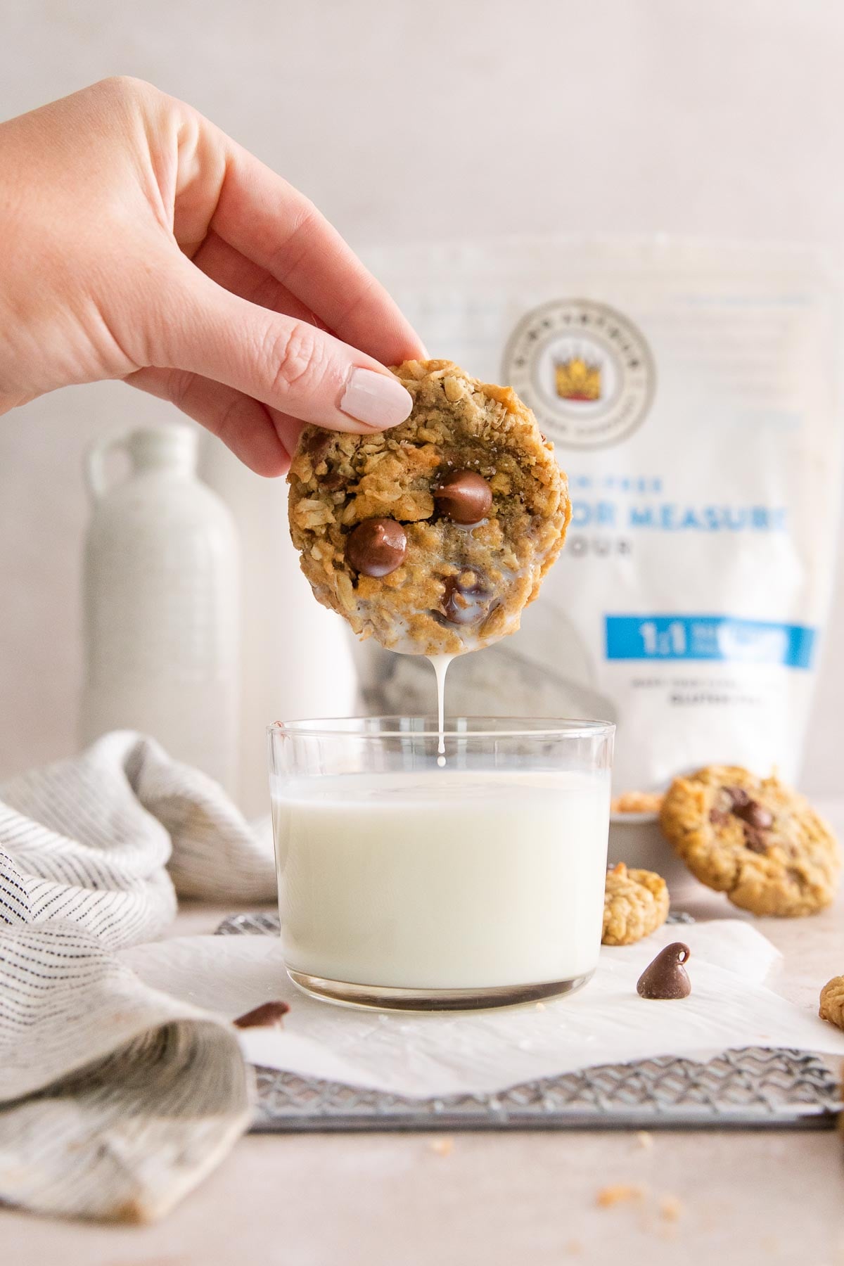 a hand dipping a cowboy cookie in a glass of milk.