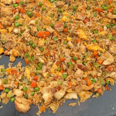 A close-up of chicken fried rice with peas, carrots, scrambled eggs, and chunks of chicken mixed with rice on a flat surface.