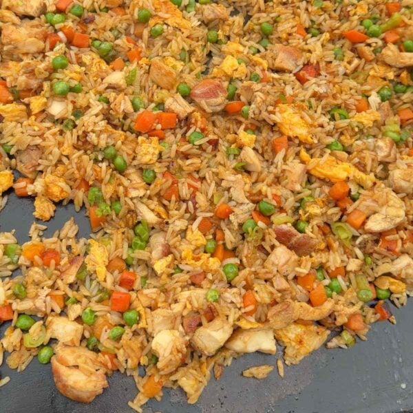A close-up of chicken fried rice with peas, carrots, scrambled eggs, and chunks of chicken mixed with rice on a flat surface.