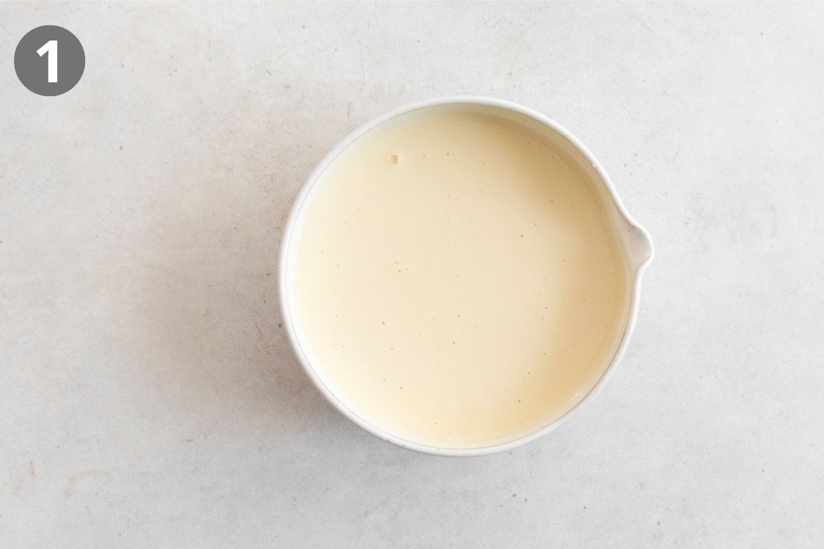 White bowl filled with smooth, creamy batter on a light gray surface. A gray circle with the number 1 is in the top left corner.