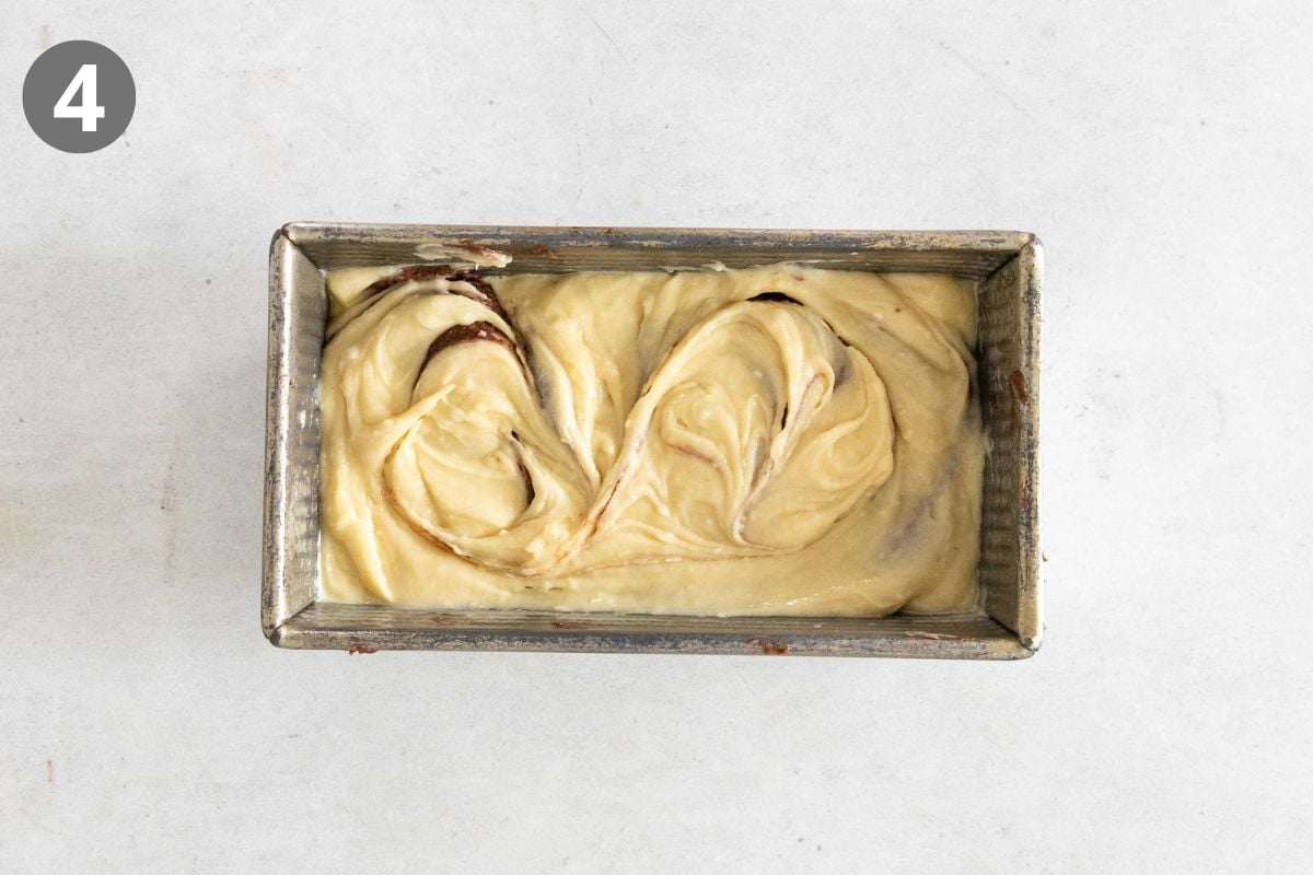 A metal loaf pan filled with swirled cake batter sits on a light surface. A 4 in a dark circle is in the top left corner, indicating this is step four in a recipe.