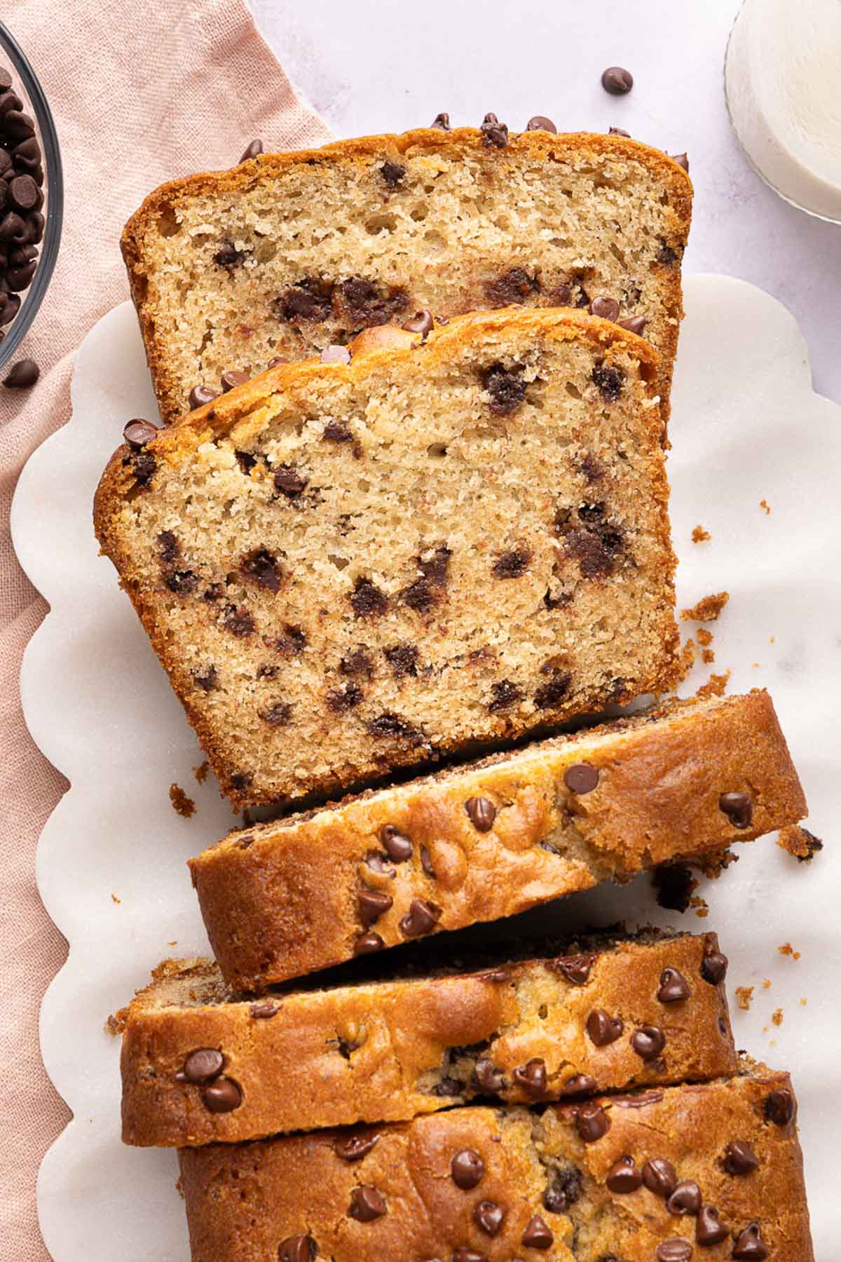 Sliced chocolate chip yogurt loaf on a white scalloped plate, with chocolate chips visible in the moist bread and some scattered on top.