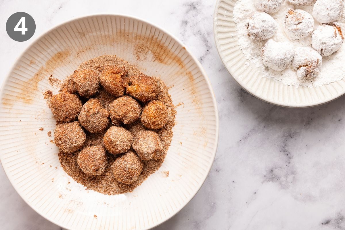 A bowl of round treats coated in cinnamon sugar, with another bowl of similar treats covered in powdered sugar nearby on a marble surface. The number 4 is in the top left corner.